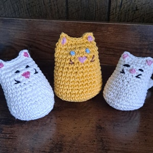 May include: Three crocheted cat toys. One is yellow, one is white, and one is white with pink accents.