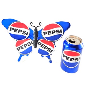 Könnte beinhalten: Ein blauer Schmetterling mit Pepsi-Logos auf seinen Flügeln und einer Pepsi-Dose.