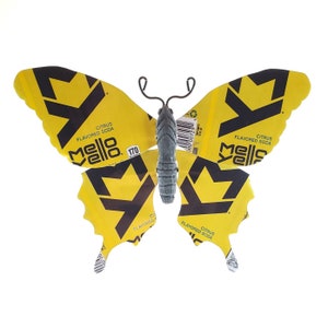 Puede incluir: Una mariposa amarilla hecha de latas de refresco Mello Yello recicladas. La mariposa tiene marcas negras y un cuerpo gris.