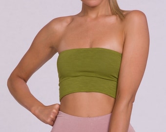 May include: A woman wearing a green tube top and dusty rose-colored biker shorts. The shorts are high-waisted and reach the mid-thigh. The top is a solid olive green. The woman is barefoot and has her hair pulled back.