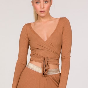 Op de afbeelding: Een tweedelige bruine outfit met een wikkel top met lange mouwen en een harembroek. De top heeft een V-hals en een striksluiting. De broek heeft een geplooide enkel en een goudkleurige tailleband. De outfit is gemaakt van een zachte, soepele stof.