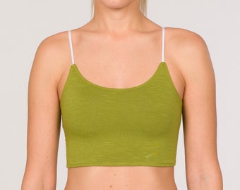 Pode incluir: Um conjunto desportivo verde-oliva de duas peças. A parte de cima é um top curto com alças brancas. As calças a condizer são de cintura alta, com cintura com cordão. A modelo usa uma scrunchie branca no cabelo.
