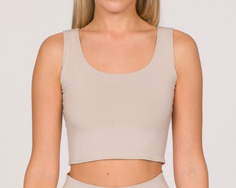 May include: A beige crop top and matching high-waisted pants. The crop top has a scoop neckline and a fitted silhouette. The pants have a wide waistband and a relaxed fit. The outfit is made of a soft, neutral-toned fabric.