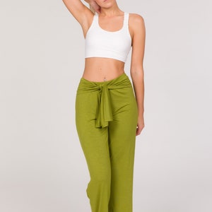 May include: A woman wearing a white sports bra and olive green trousers. The trousers have a tie at the waist. The woman has blonde hair tied back.