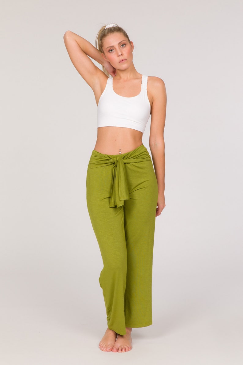 May include: A woman wearing a white sports bra and olive green trousers. The trousers have a tie at the waist. The woman has blonde hair tied back.