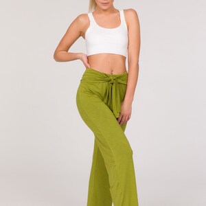 May include: A woman wearing a white sports bra and olive green wide-leg trousers with a tie waist. The trousers are a solid colour and have a relaxed fit. The model is standing barefoot against a white background.