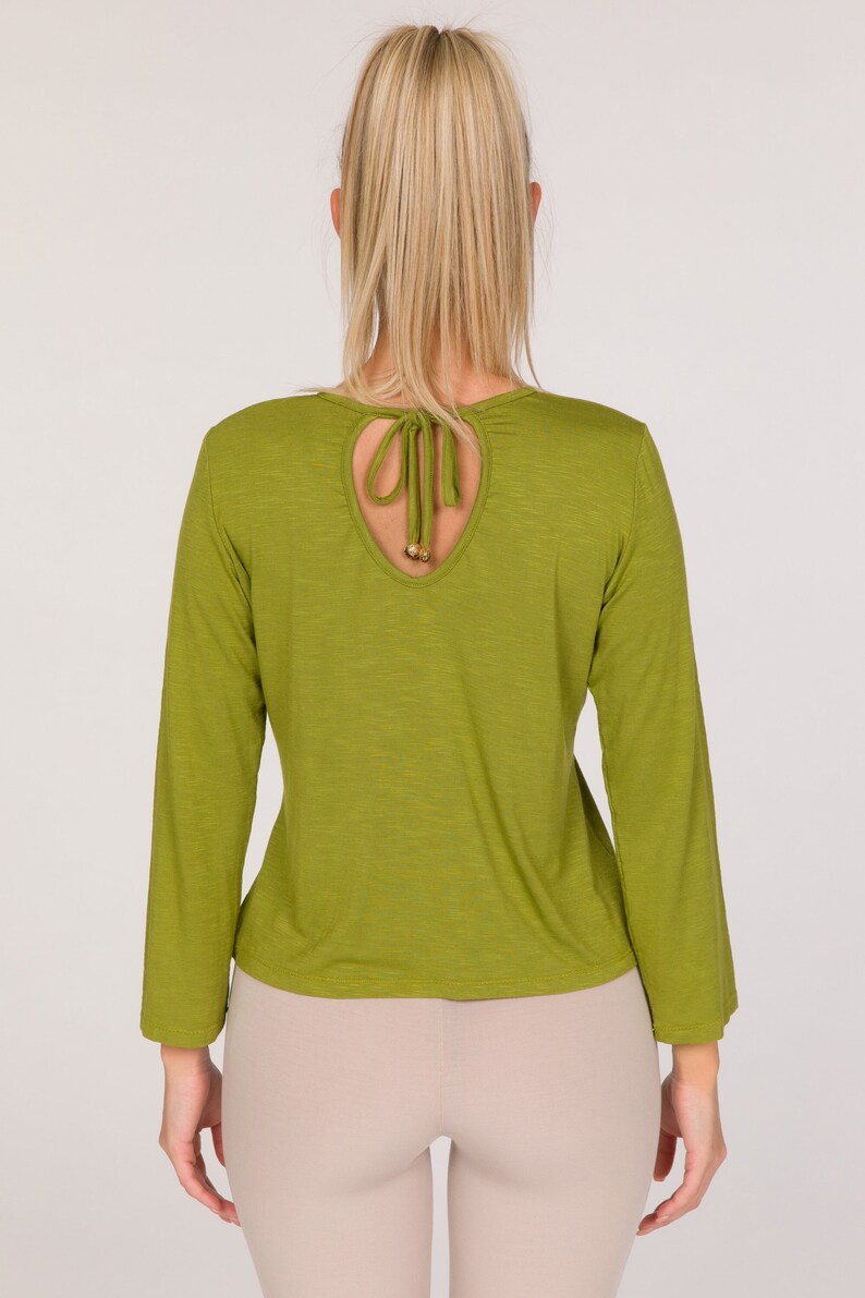 Puede incluir: Top verde oliva de manga larga con detalle de espalda con abertura. El top presenta un cuello redondo y mangas largas. La abertura est&aacute; atada con tela a juego y cuentas doradas. La modelo lleva leggings color beige.