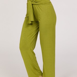 May include: Olive green palazzo trousers with a high waist and a tie detail. The trousers are made of a soft, flowing fabric and have a wide leg. The model is wearing a white crop top. The trousers are a solid colour.
