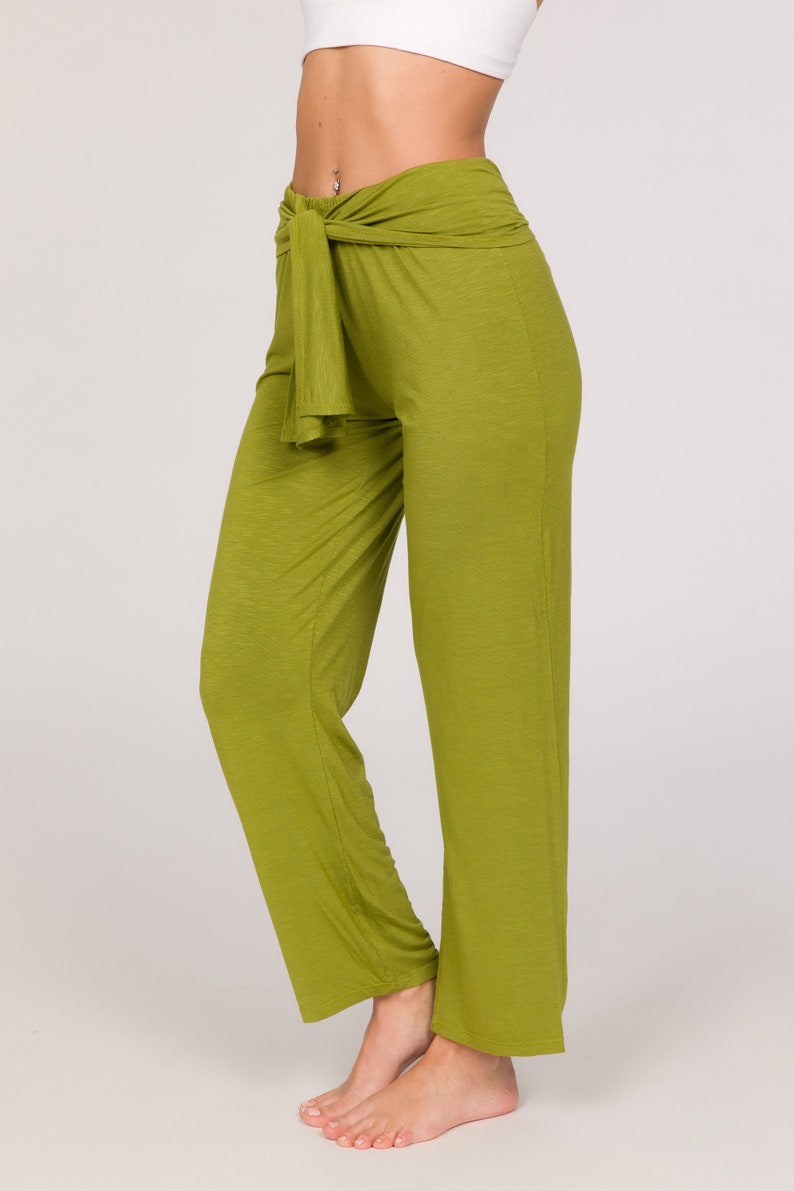 May include: Olive green palazzo trousers with a high waist and a tie detail. The trousers are made of a soft, flowing fabric and have a wide leg. The model is wearing a white crop top. The trousers are a solid colour.