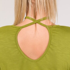 Puede incluir: Primer plano de una camisa verde de manga larga con un dise&ntilde;o de espalda con abertura. La camisa tiene un escote redondo y un detalle de correas cruzadas en la espalda. La tela tiene una sutil apariencia texturizada.