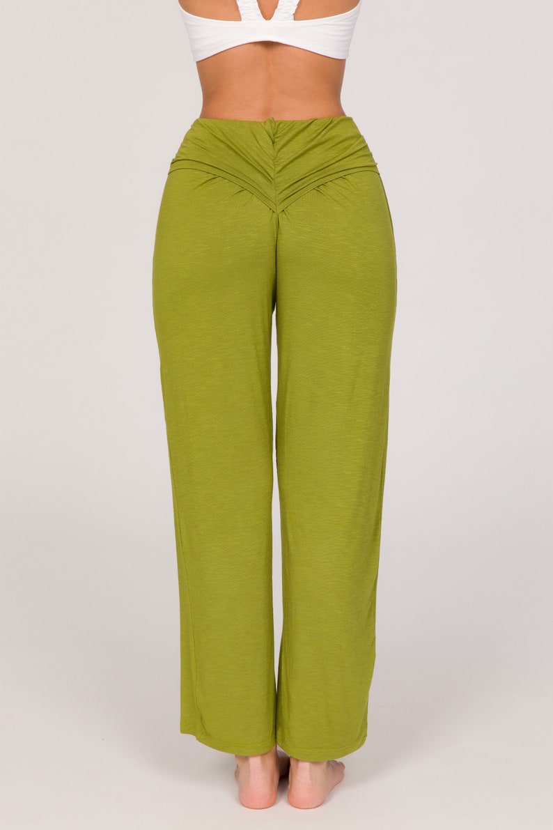 May include: Olive green wide-leg trousers with a ruched back waist detail. The model is wearing a white top. The trousers are made from a soft, flowing fabric. The trousers are a vibrant shade of green.