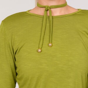 Puede incluir: Top verde oliva de manga larga con gargantilla a juego. La gargantilla tiene cierre de lazo y detalles decorativos de bolas doradas. El top tiene cuello redondo y un aspecto texturizado.