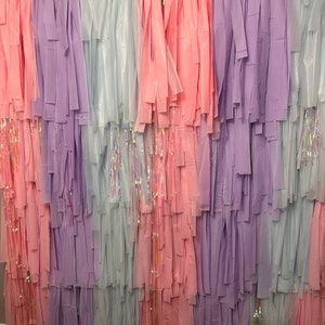 Puede incluir: Un telón de fondo de serpentinas de papel de seda superpuestas en tonos de azul claro, lavanda y rosa. Las serpentinas están dispuestas en filas verticales, creando un fondo colorido y festivo.