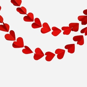 May include: Two strands of red paper heart garlands, each with multiple heart shapes, are suspended against a white background. The hearts are evenly spaced and create a decorative, romantic aesthetic, perfect for Valentine's Day or other celebrations.