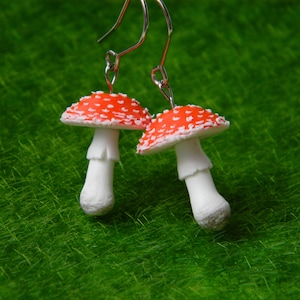 May include: A pair of red and white mushroom earrings with silver hooks. The mushrooms have white spots on the red caps and white stems.