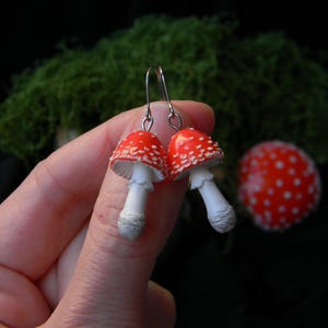 Op de afbeelding: Een paar rode en witte paddenstoel oorbellen met zilveren haken. De paddenstoelen hebben witte stelen en rode hoeden met witte stippen.