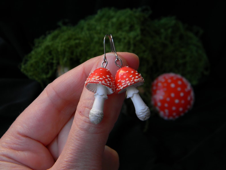 Op de afbeelding: Een paar rode en witte paddenstoel oorbellen met zilveren haken. De paddenstoelen hebben witte stelen en rode hoeden met witte stippen.