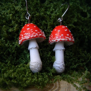 Op de afbeelding: Een paar rode en witte paddenstoel oorbellen. De paddenstoelen hebben een witte steel en een rode dop met witte stippen.