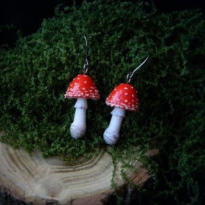 Op de afbeelding: Een paar rode en witte paddenstoel oorbellen met zilveren haakjes. De paddenstoelen hebben witte stelen en rode hoeden met witte stippen.