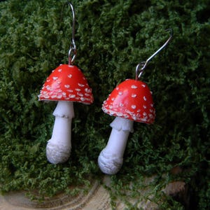Op de afbeelding: Een paar rode en witte paddenstoel oorbellen met zilveren haakjes. De paddenstoelen hebben witte stippen en een witte steel.
