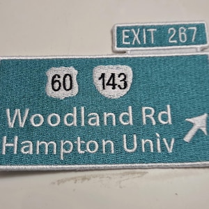 May include: Embroidered teal patch resembling a highway sign. Features white text indicating "EXIT 267", "60", "143", "Woodland Rd", and "Hampton Univ", with a white arrow. The patch has a white border.