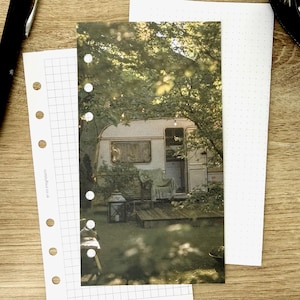 May include: A rectangular planner insert featuring a photographic print of a vintage camper parked under trees. The paper has six circular punch holes along the left edge and the text sortstuffout.co.uk printed vertically near the holes.