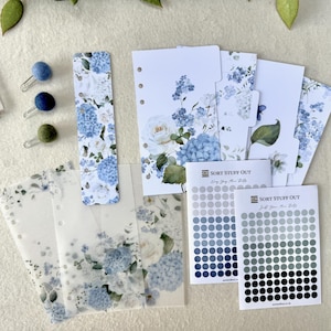 May include: A collection of stationery items featuring a floral design with blue hydrangeas and white roses. Includes a bookmark, planner dividers, stickers, and decorative paper clips. The text "SORT STUFF OUT" is visible on the stickers.