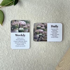 May include: Two white cards with rounded corners. One card reads "Weekly" with a list of tasks. The other card reads "Daily" with a list of tasks. Both cards have a photo of potted flowers.