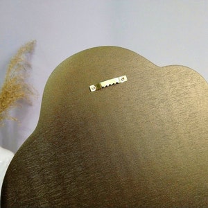 May include: The back of a gold-colored, cloud-shaped wall hanging with a metal hanging hook.