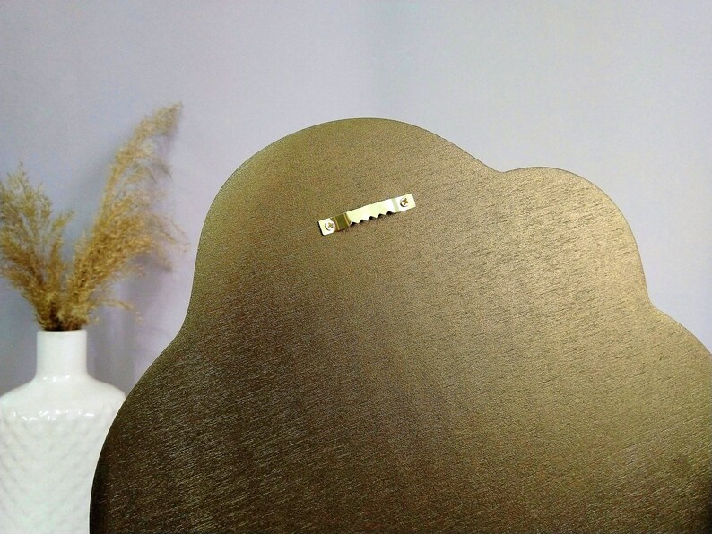 May include: The back of a gold-colored, cloud-shaped wall hanging with a metal hanging hook.