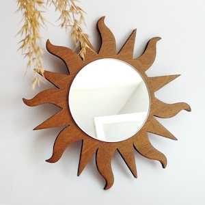 May include: A brown wooden sunburst mirror with a round mirror in the center. The mirror is reflecting a white ceiling.