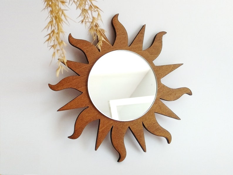 May include: A brown wooden sunburst mirror with a round mirror in the center. The mirror is reflecting a white ceiling.