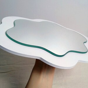 May include: A cloud-shaped mirror with a white frame and a clear glass mirror. The mirror has an organic shape, and the white frame provides a clean, modern aesthetic. The mirror is a decorative item.