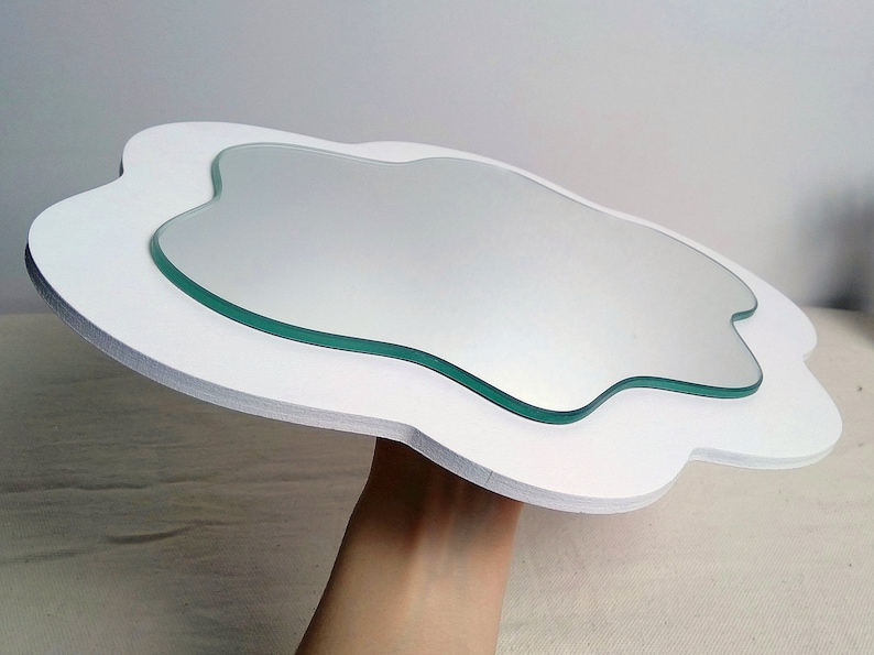May include: A cloud-shaped mirror with a white frame and a clear glass mirror. The mirror has an organic shape, and the white frame provides a clean, modern aesthetic. The mirror is a decorative item.
