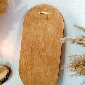 May include: The back of a wooden oval-shaped mirror with a brass hanging hook.