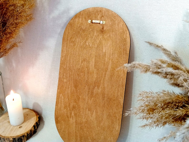 May include: The back of a wooden oval-shaped mirror with a brass hanging hook.