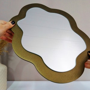 May include: A gold-colored, cloud-shaped mirror with a smooth, reflective surface. The mirror has a unique, organic shape and a slightly textured frame.