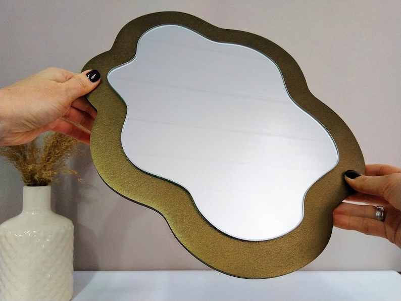 May include: A gold-colored, cloud-shaped mirror with a smooth, reflective surface. The mirror has a unique, organic shape and a slightly textured frame.