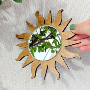 May include: A wooden sun-shaped mirror with a round mirror in the center. The mirror reflects a green plant.