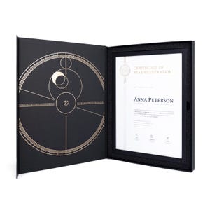 Può includere: Cartella di presentazione nera aperta con un certificato all'interno. Il certificato è incorniciato in nero e riporta la scritta "Certificate of Star Registration" e il nome "Anna Peterson". L'interno della copertina presenta un disegno celeste dorato.