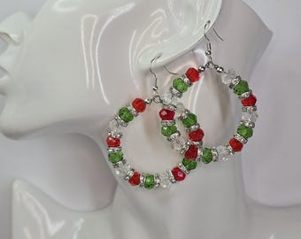 May include: Hoop earrings featuring red, green, and clear beads. The earrings have silver-tone metal hooks and are displayed on a white mannequin head. The beads are arranged in alternating colours around the hoops.