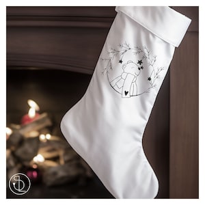 May include: White Christmas stocking with a black and white embroidered design of a bear wearing a scarf and looking up at stars in a wreath of pine branches.