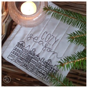 May include: White quilted fabric with black embroidery of a city skyline and the words "cozy season".