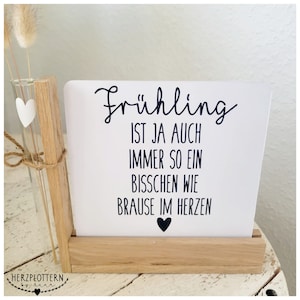 Puede incluir: Un letrero de madera blanco con texto negro que dice "Frühling ist ja auch immer so ein bisschen wie brause im Herzen" con un pequeño corazón negro en la parte inferior.