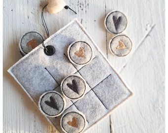 May include: A felt tic-tac-toe game with a grey background and black lines. The game pieces are round and have embroidered hearts in gold and black.