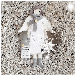 May include: A white felt angel with grey wings, a grey scarf with a gold star, and a white dress with a pocket. The angel is holding a white star with a black outline and a small white heart. The angel is surrounded by a wreath of white dried flowers. The text on the sign says "von Himmel hoch da komm ich her".
