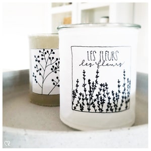 Könnte beinhalten: Zwei weiße Glaskerzenbehälter mit schwarzen Blumenmustern. Der Behälter rechts trägt den Text "LES FLEURS les fleurs".