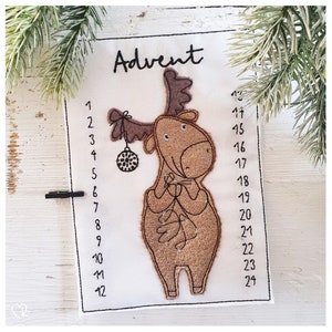 Op de afbeelding: Een witte vilt adventskalender met een bruine eland die een kerstbal vasthoudt. De nummers 1 tot en met 24 staan ​​gedrukt aan de rechterkant van de kalender. Het woord "Advent" staat ​​bovenaan de kalender gedrukt.