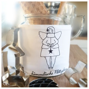 Könnte beinhalten: Ein weißes Glas mit einem schwarzen und weißen gestickten Engelmotiv auf der Vorderseite. Das Glas hat den Text "himmlische Plätzchen" auf dem Boden.