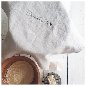 May include: A white linen kitchen towel with the text "Momentchen bitte" embroidered in black with a small heart.